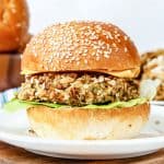 White plate with lentil cheeseburger on a bun on a wooden board.