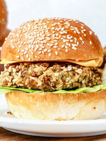 White plate with lentil cheeseburger on a bun on a wooden board.