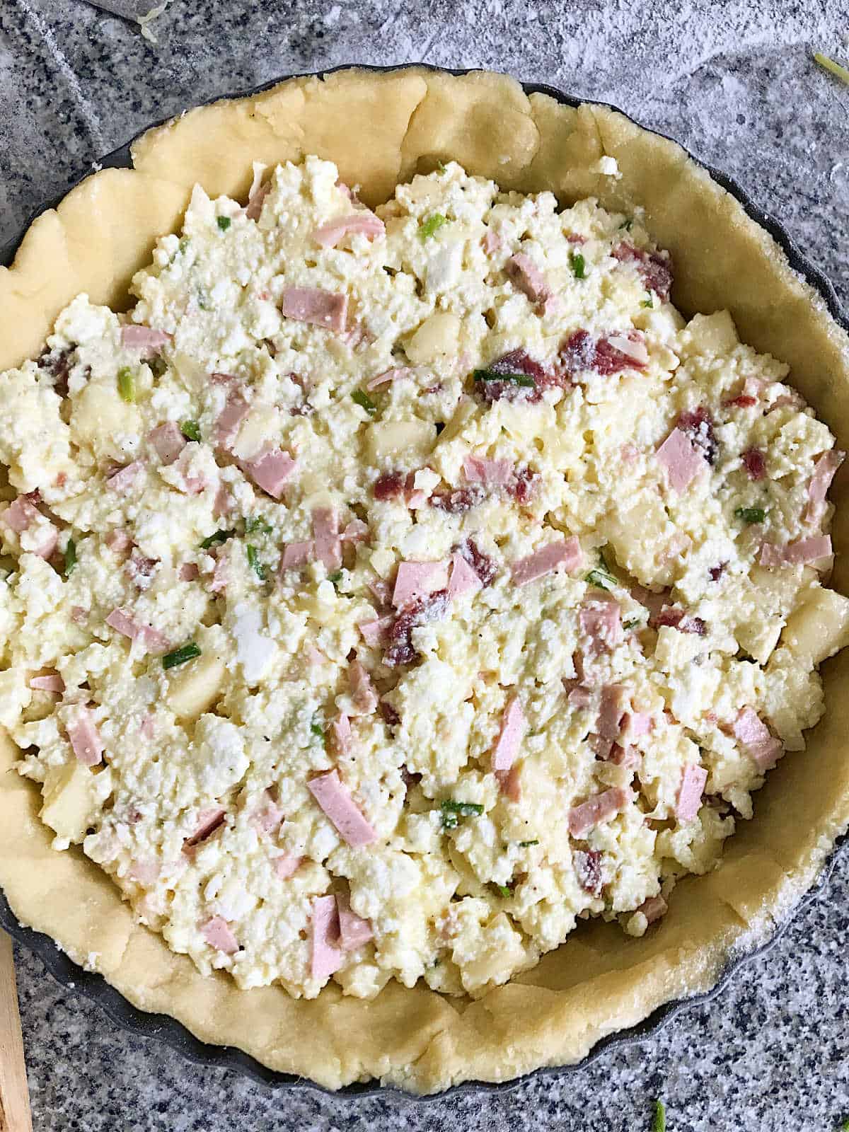 Round unbaked pie crust with ricotta, cold meats filling on a grey surface