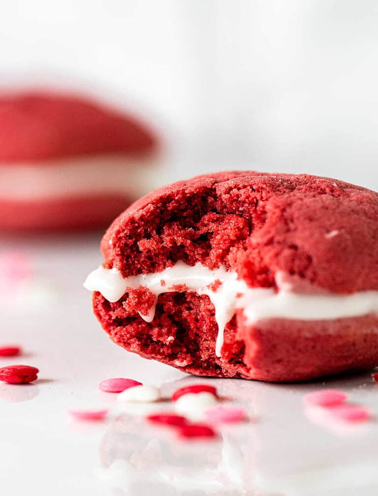 Close up of eaten red velvet whoopie pie, white marble surface, pink and red confetti around