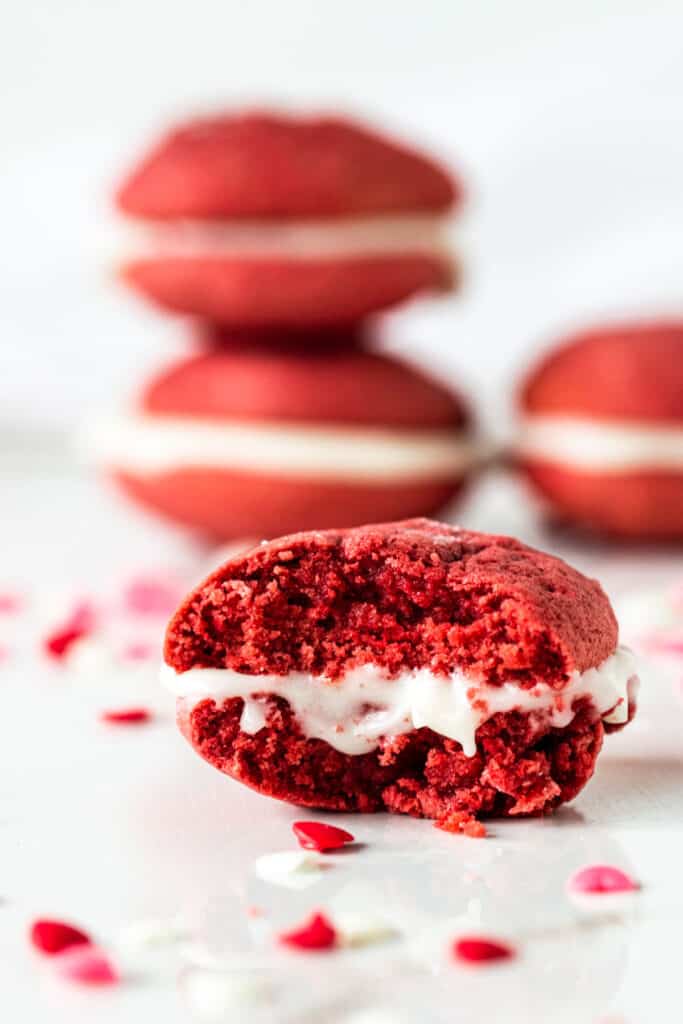 Eaten red whoopie pie on white surface with red confetti, more pies in background