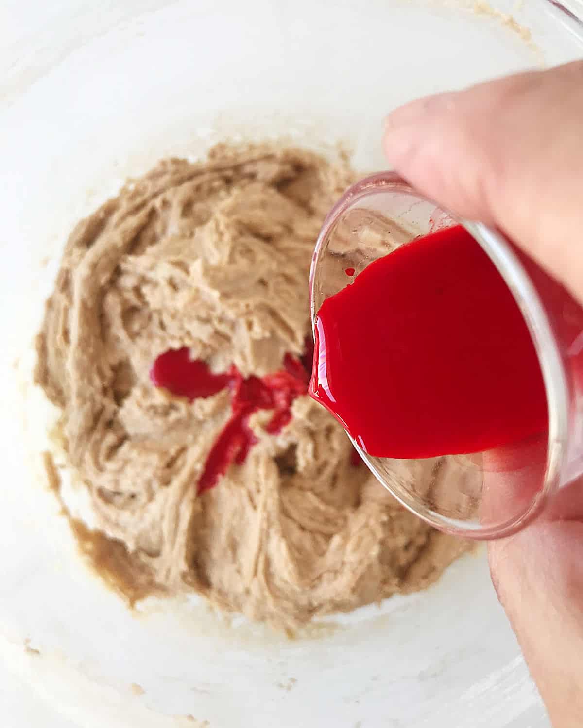Adding red food coloring to cake batter in a glass bowl.