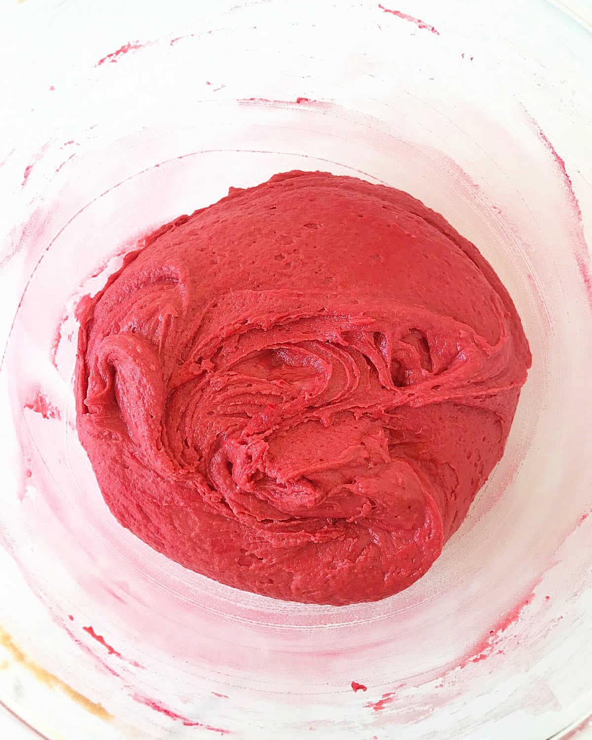Red-colored batter in a glass bowl on a white surface.