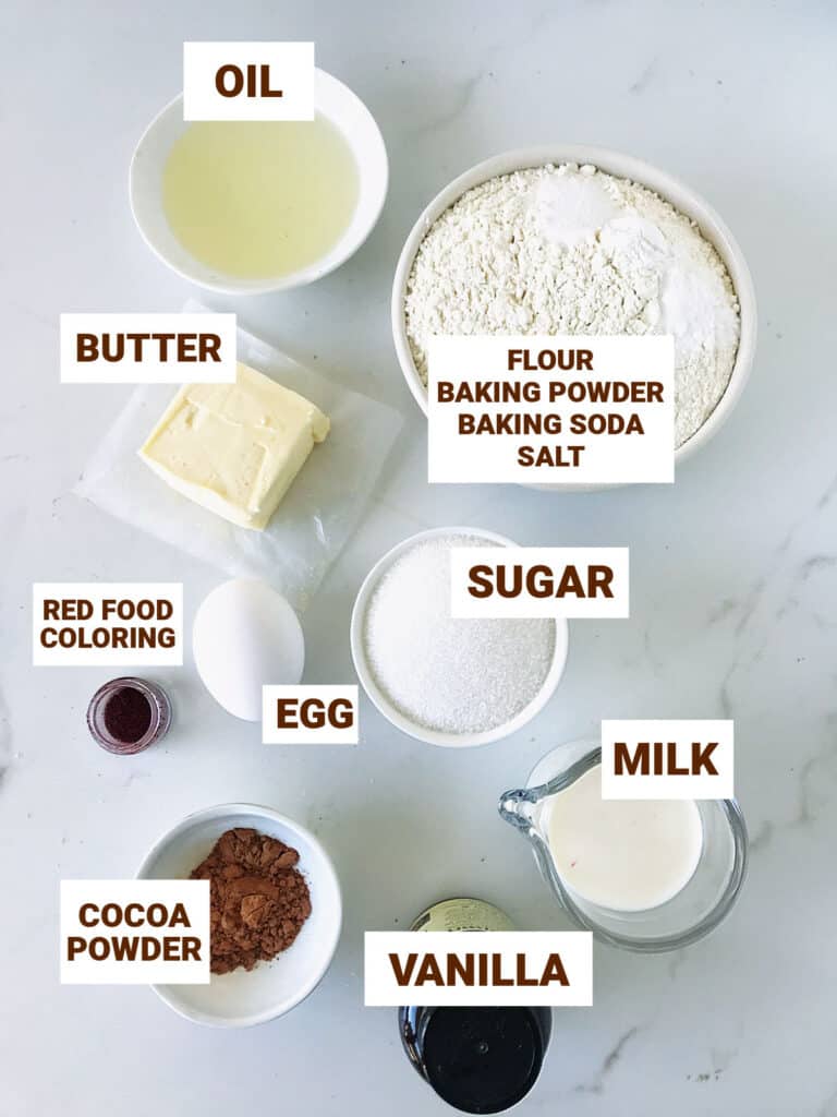 Bowls with ingredients for red velvet whoppie pies on a white surface, including oil, butter, cocoa powder