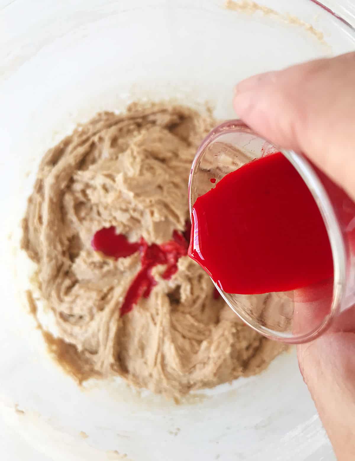 Adding liquid red coloring to light chocolate batter in a bowl