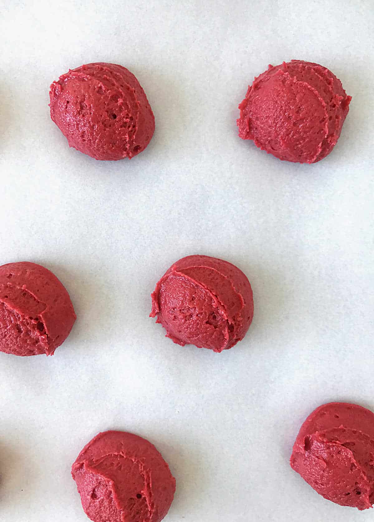 Mounds of red velvet whoopie pie batter on parchment paper ready to be baked