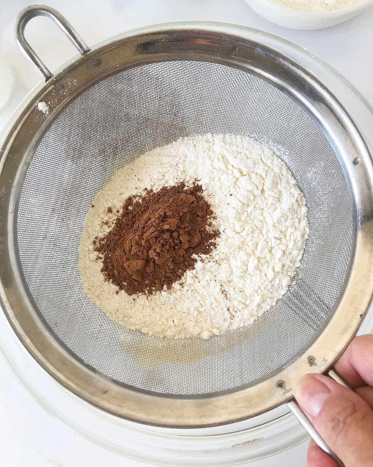 Sifting flour and cocoa powder over a glass bowl.