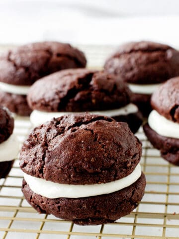 A wire rack with several chocolate whoopie pies with creamy filling