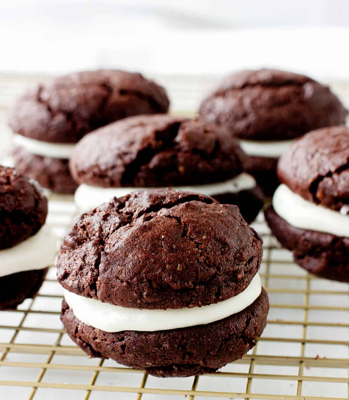 Several chocolate whoopie pies with creamy filling on a golden wire rack