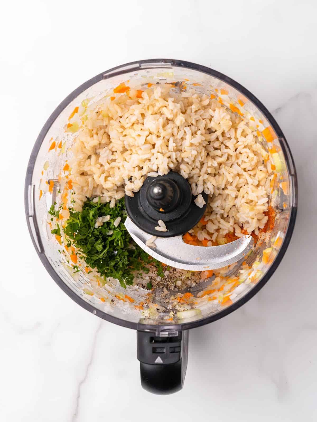 Rice and parsley added to food processor bowl with chopped vegetables. White marble surface. 