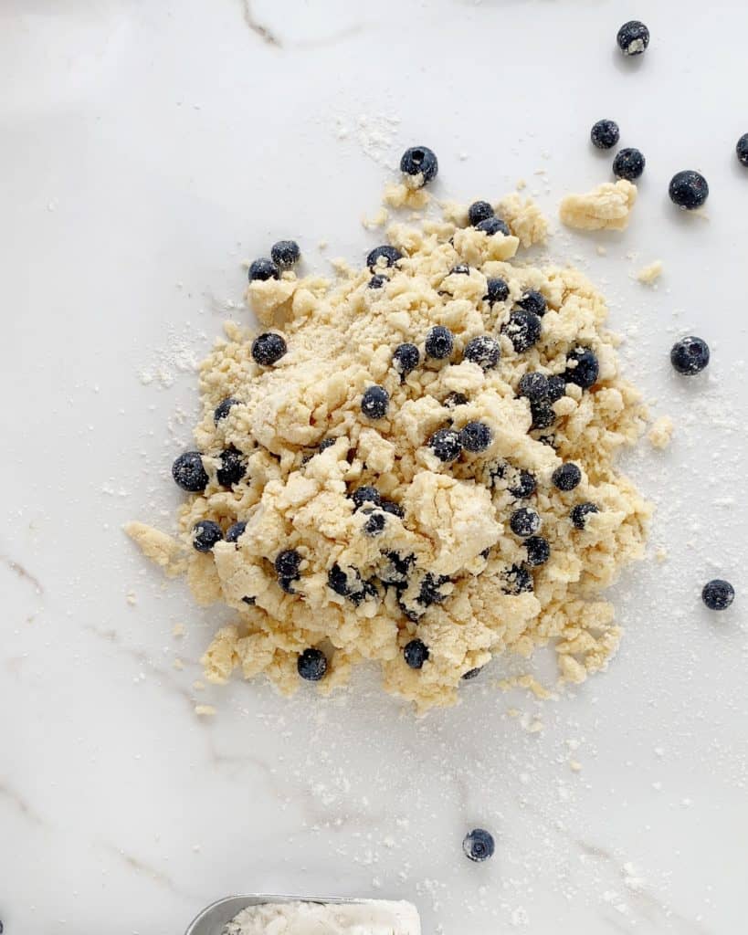 Shaggy blueberry scone dough dumped on a white marble surface.