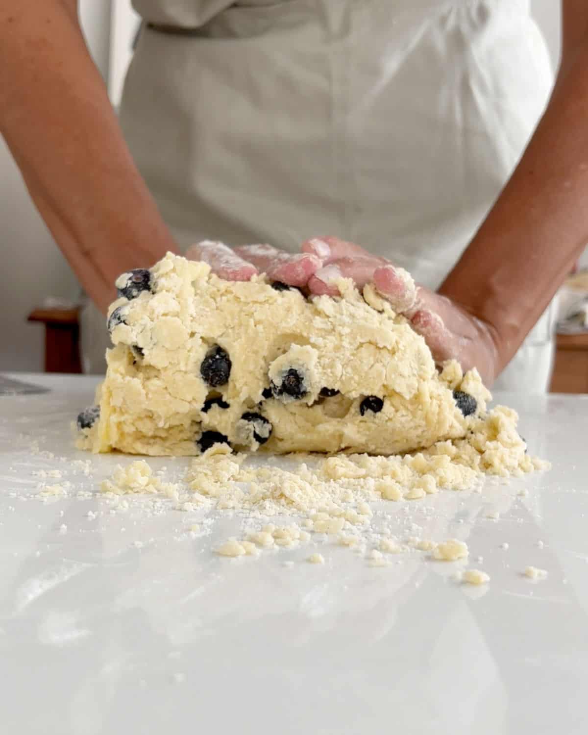 Front view of person integrating a blueberry scone dough on white marble surface.