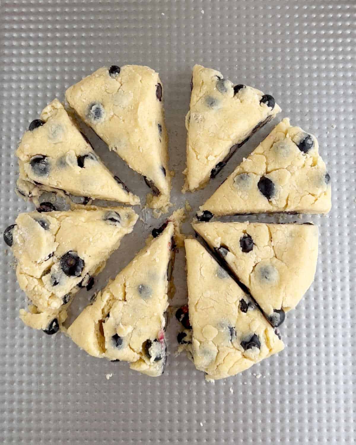 Metal sheet with round of blueberry scones cut into triangles.