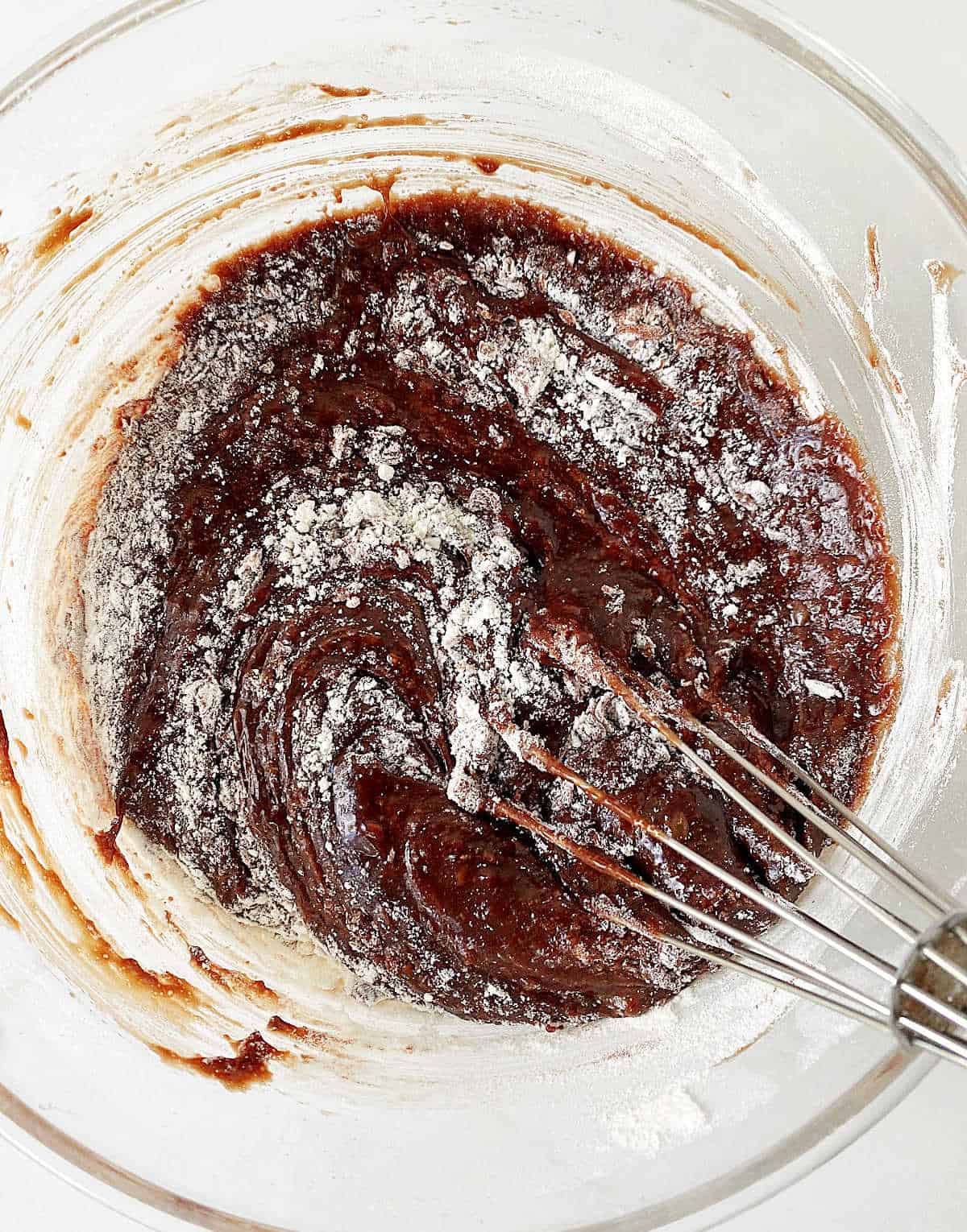 Whisking flour into brownie batter in a glass bowl.