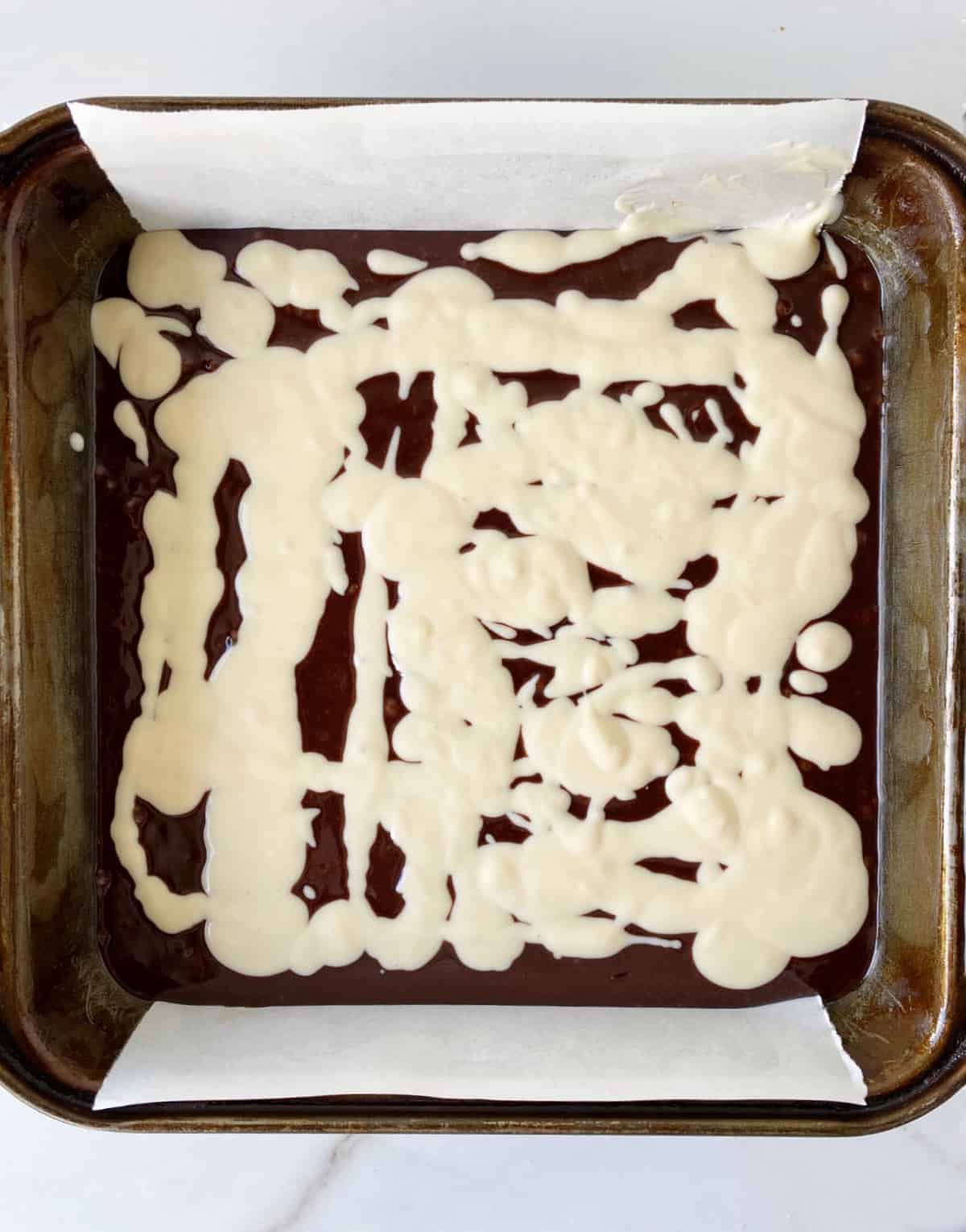Top view of brownie cheesecake batters in a metal square pan.