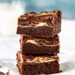 stack of three cheesecake brownies on white surface, blueish background
