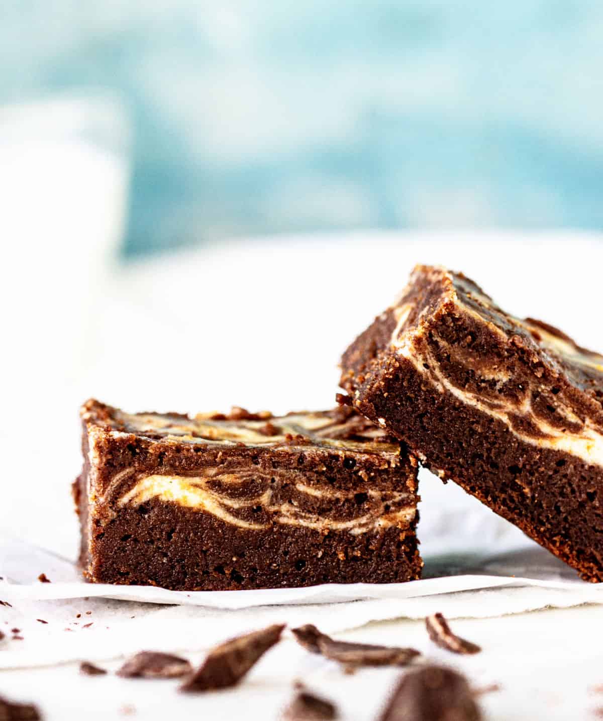 Two brownies leaning onto each other, white blue background, chocolate pieces around