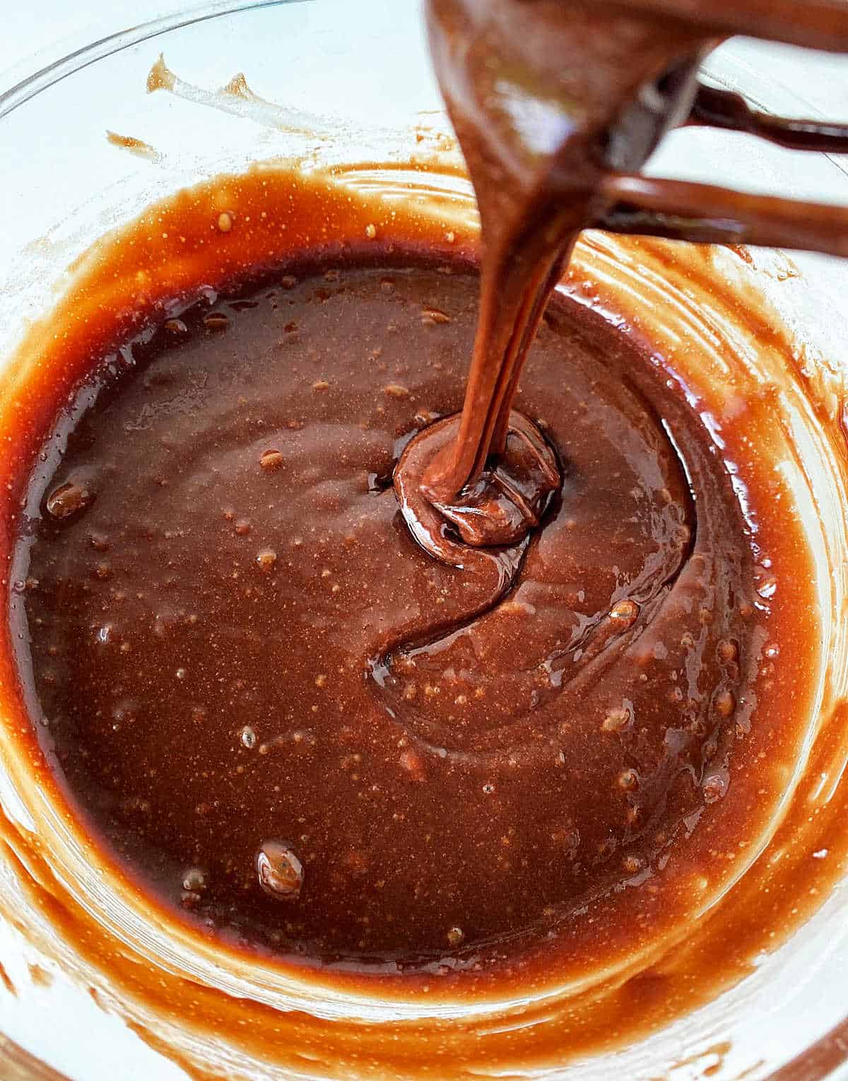 Chocolate brownie batter close-up on a glass bowl with a whisk.