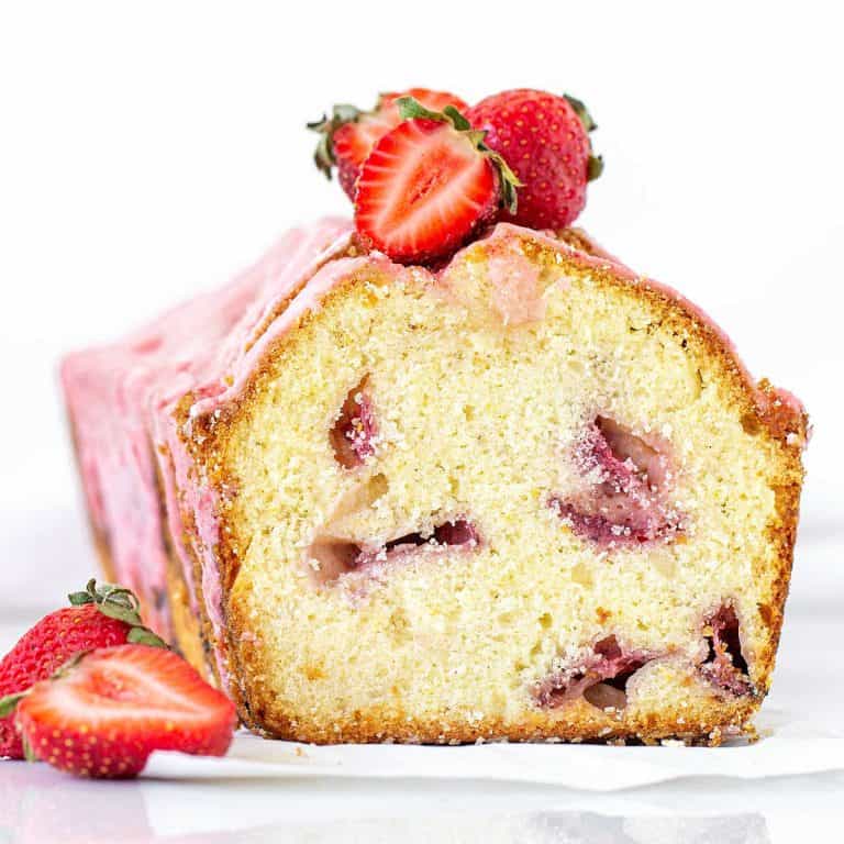 A cut loaf of strawberry pound cake, with a pink glaze and fresh strawberries. White background.