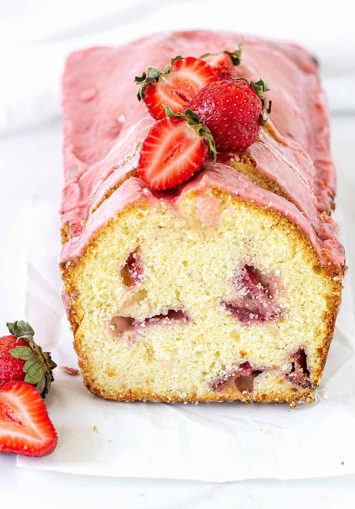 Cut loaf of pink glazed strawberry pound cake on white surface.