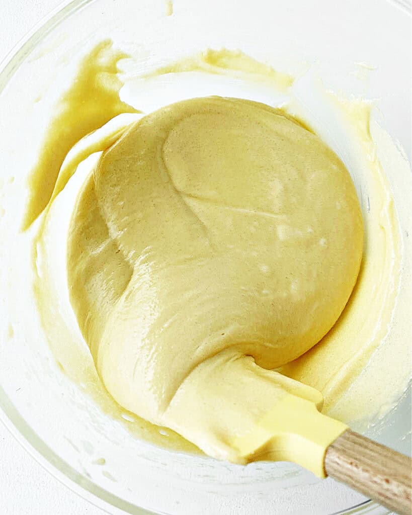 Yellow spatula folding cake batter in a glass bowl.