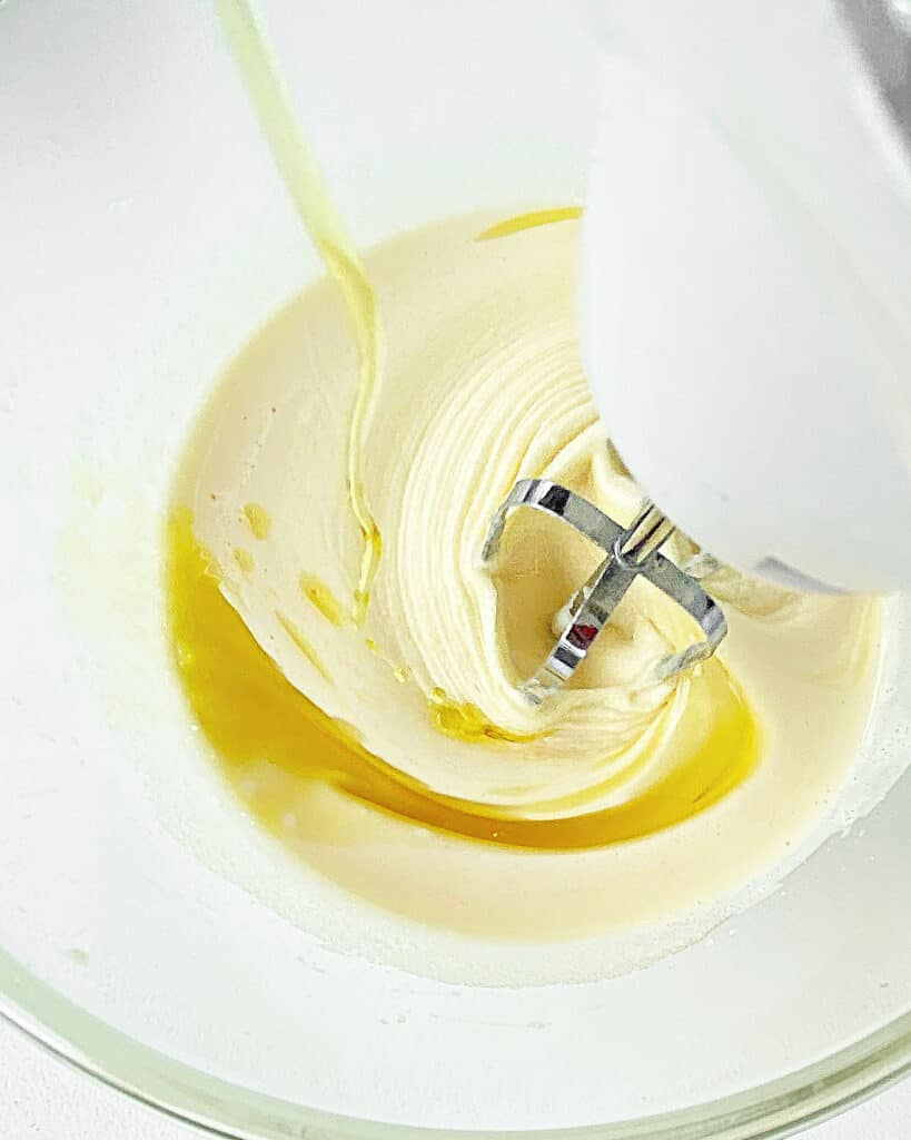 Adding oil to cake batter in glass bowl while beating.