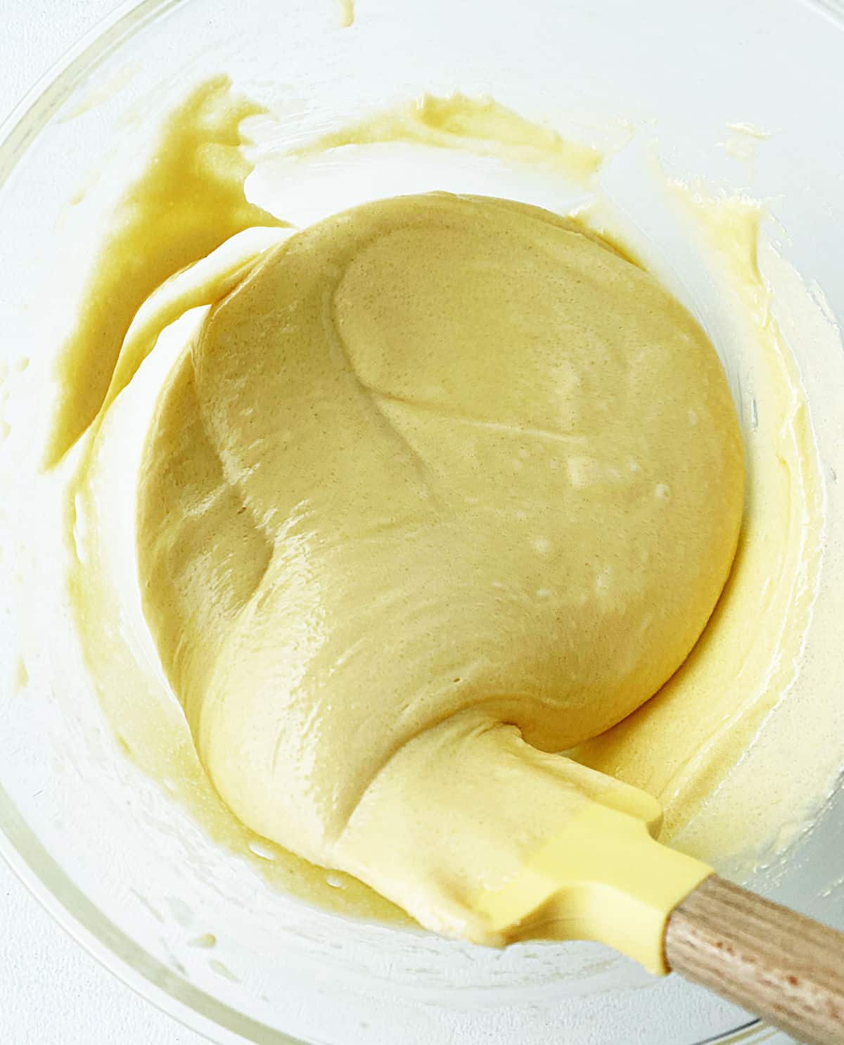 Yellow spatula mixing cake batter in a glass bowl