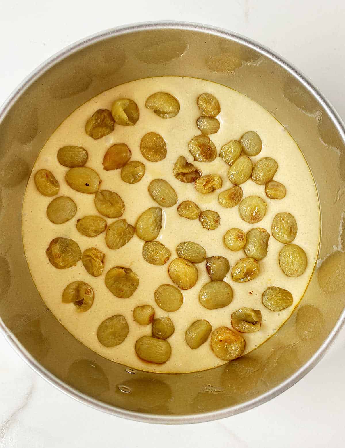 Top view of round cake pan with batter and grapes