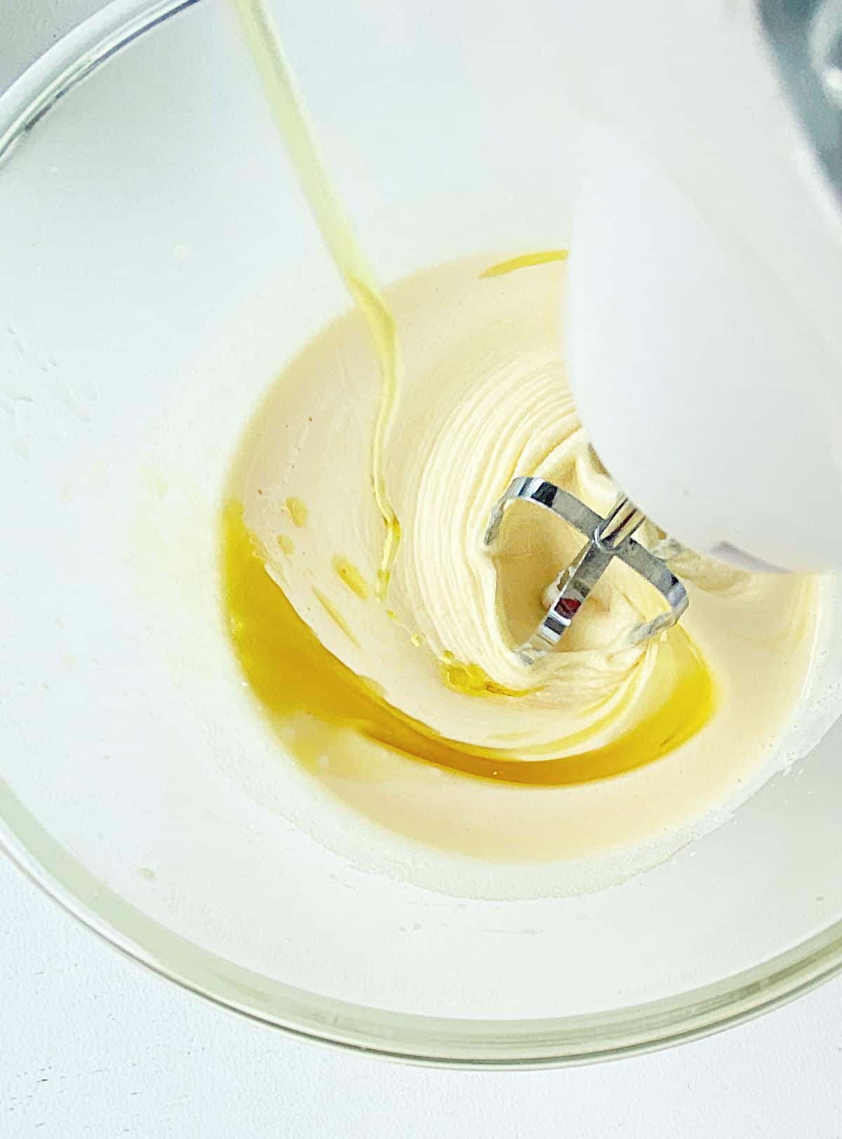 Adding oil to cake batter in glass bowl while beating