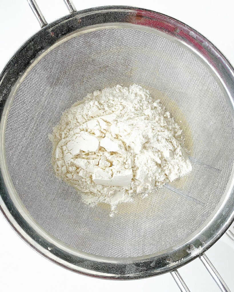 Top view of metal sifter with flour. White surface.