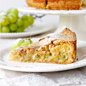 Close up slice of grape cake on a white plate. White background with grapes and cake stand.