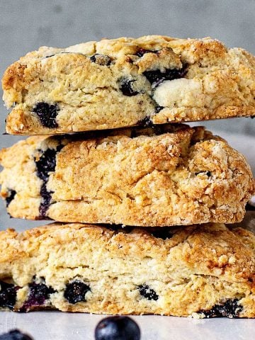 Three blueberry scones stacked on a white marble surface with greyish blue background.