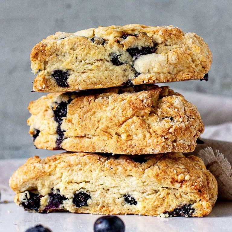 Three blueberry scones stacked on a white marble surface with greyish blue background.