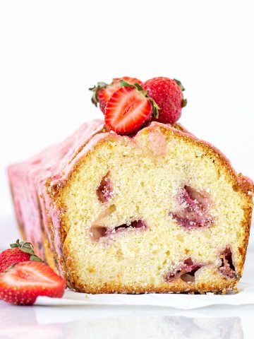 Front view of cut pound cake with strawberries and pink glaze; white background