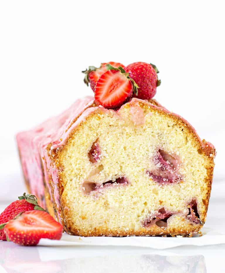Front view of cut pound cake with strawberries and pink glaze; white background
