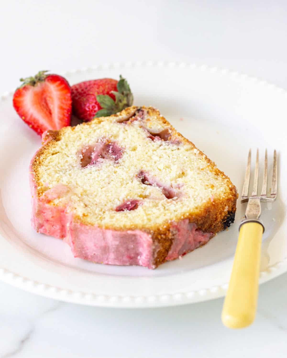 Slice of strawberry pound cake on a white plate with a yellow fork. 
