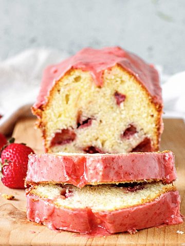 Pink glazed strawberry pound cake, whole and sliced on wooden board