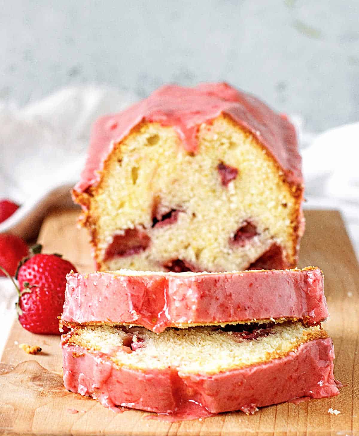 Pink glazed strawberry pound cake, whole and sliced on wooden board
