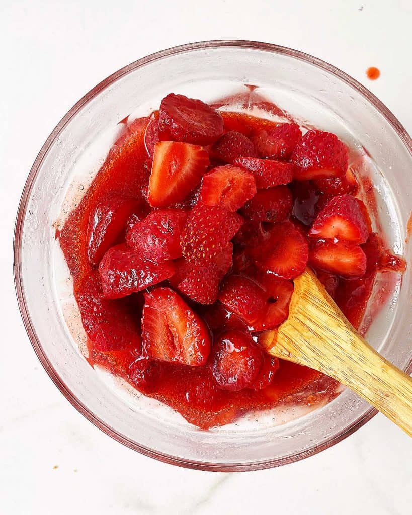 Pieces of fresh strawberries added to a glass bowl with strawberry sauce. Wooden spoon inside.