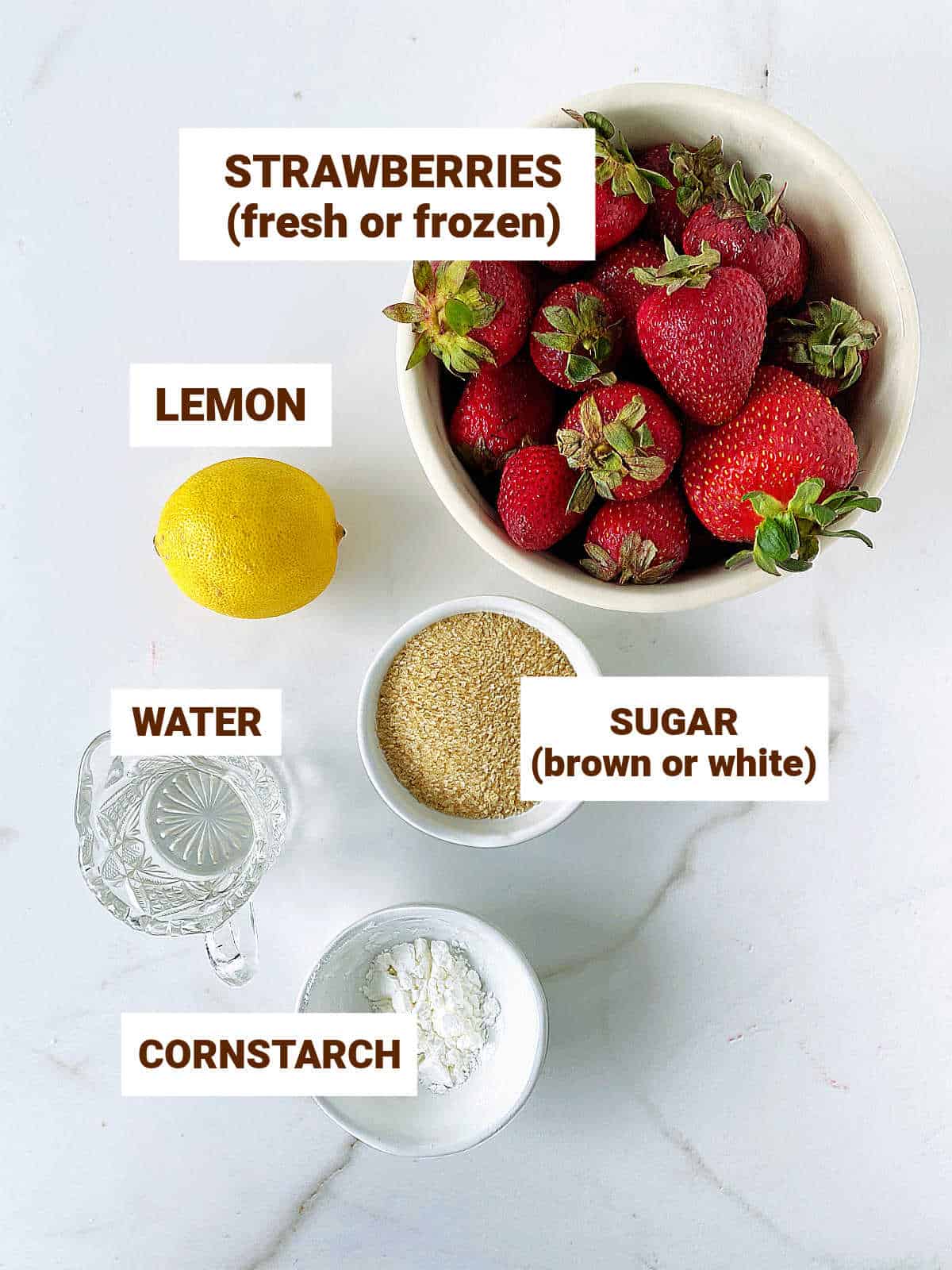 White surface with ingredients for strawberry sauce including whole lemon and brown sugar