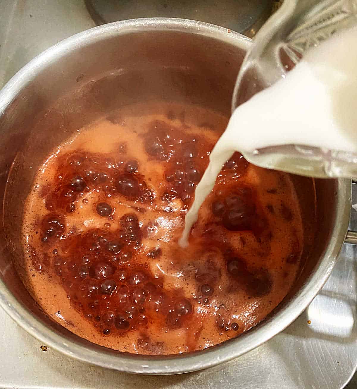 Adding white liquid to saucepan with boiling stawberries and liquid