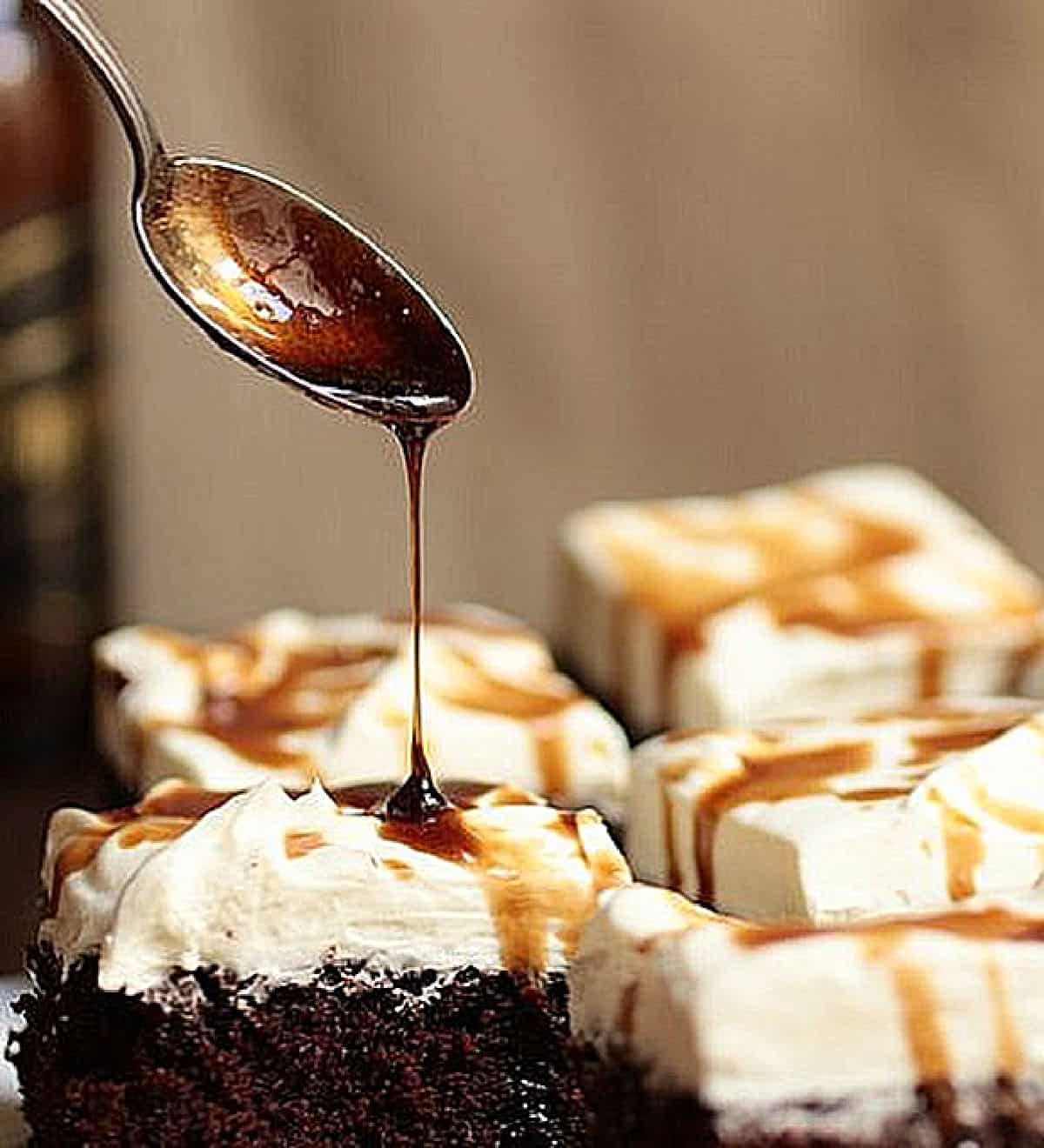 Pouring stout syrup with a spoon on cream topped chocolate cake; brown background