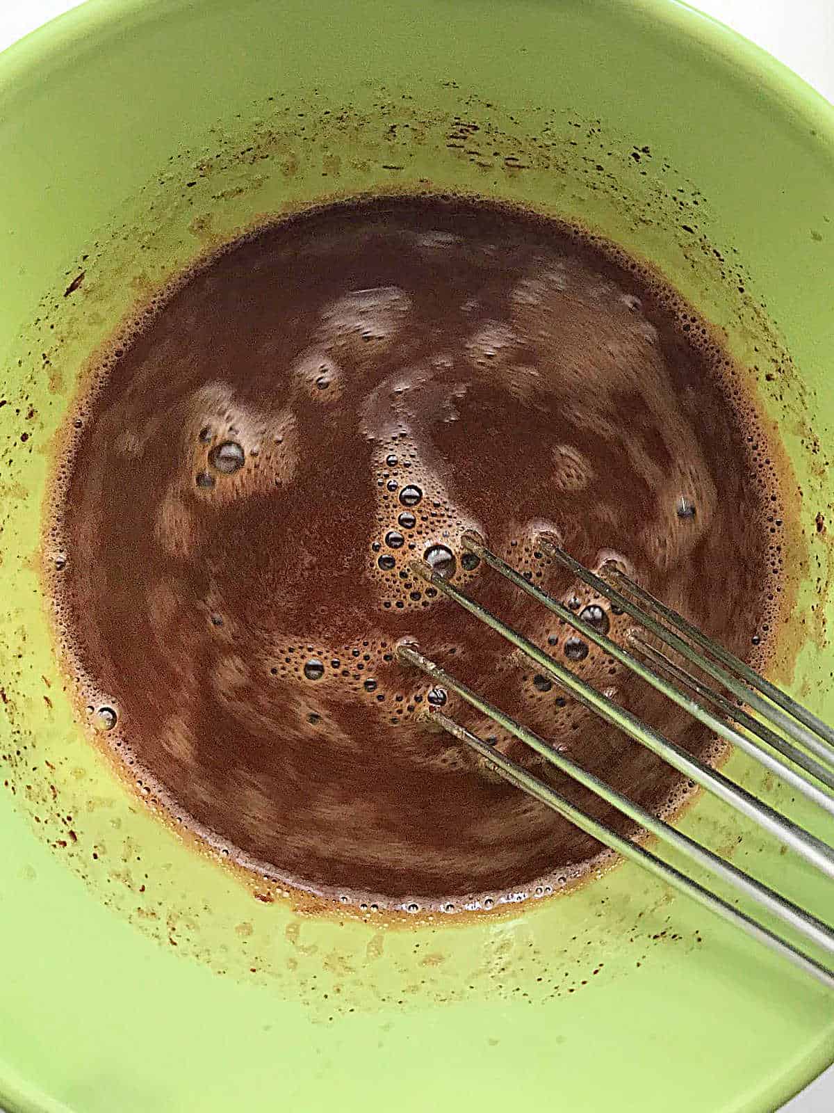 Green bowl with chocolate custard mixture and whisk.