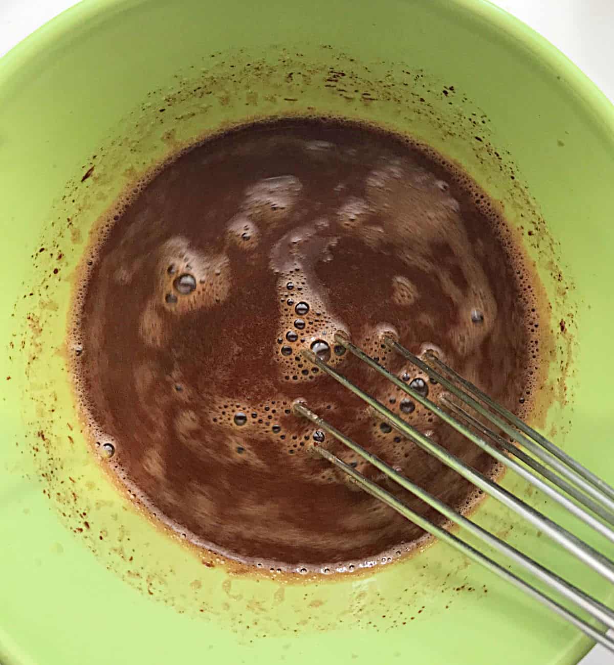 Green bowl with liquid chocolate mixture and whisk