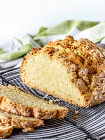 Cut loaf of soda bread and slices on wire rack with greeen kitchen towels