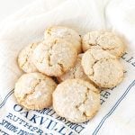 Several almond crinkled cookies piled on a white and blue kitchen towel.