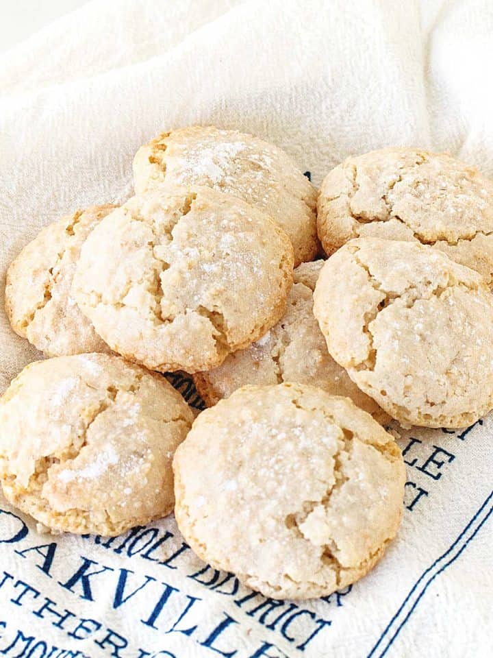 Several almond crinkled cookies piled on a white and blue kitchen towel.
