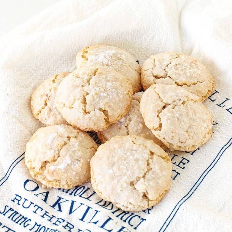Several almond crinkled cookies piled on a white and blue kitchen towel.