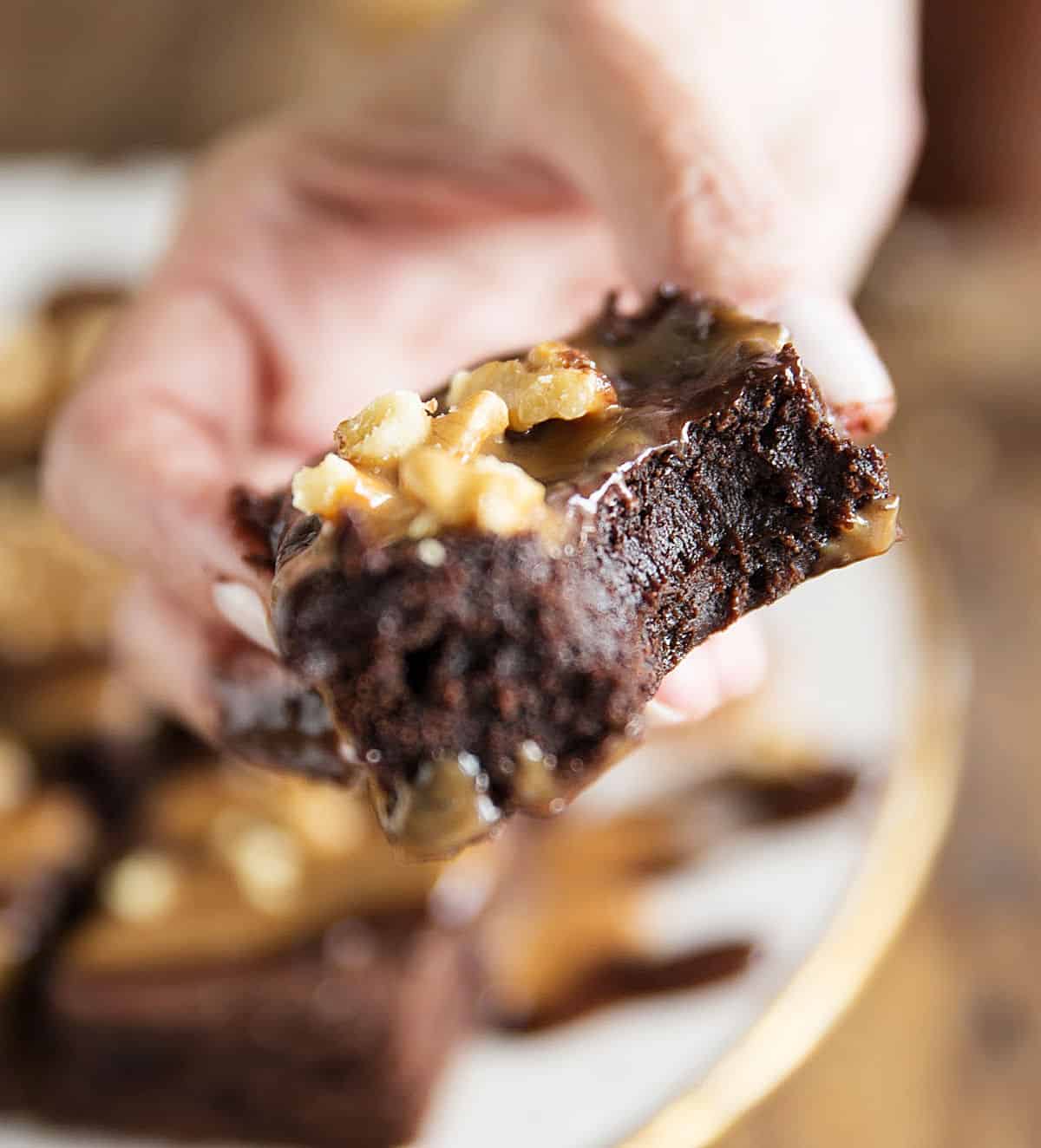 Hand holding bitten fudgy brownie with walnuts on top. 