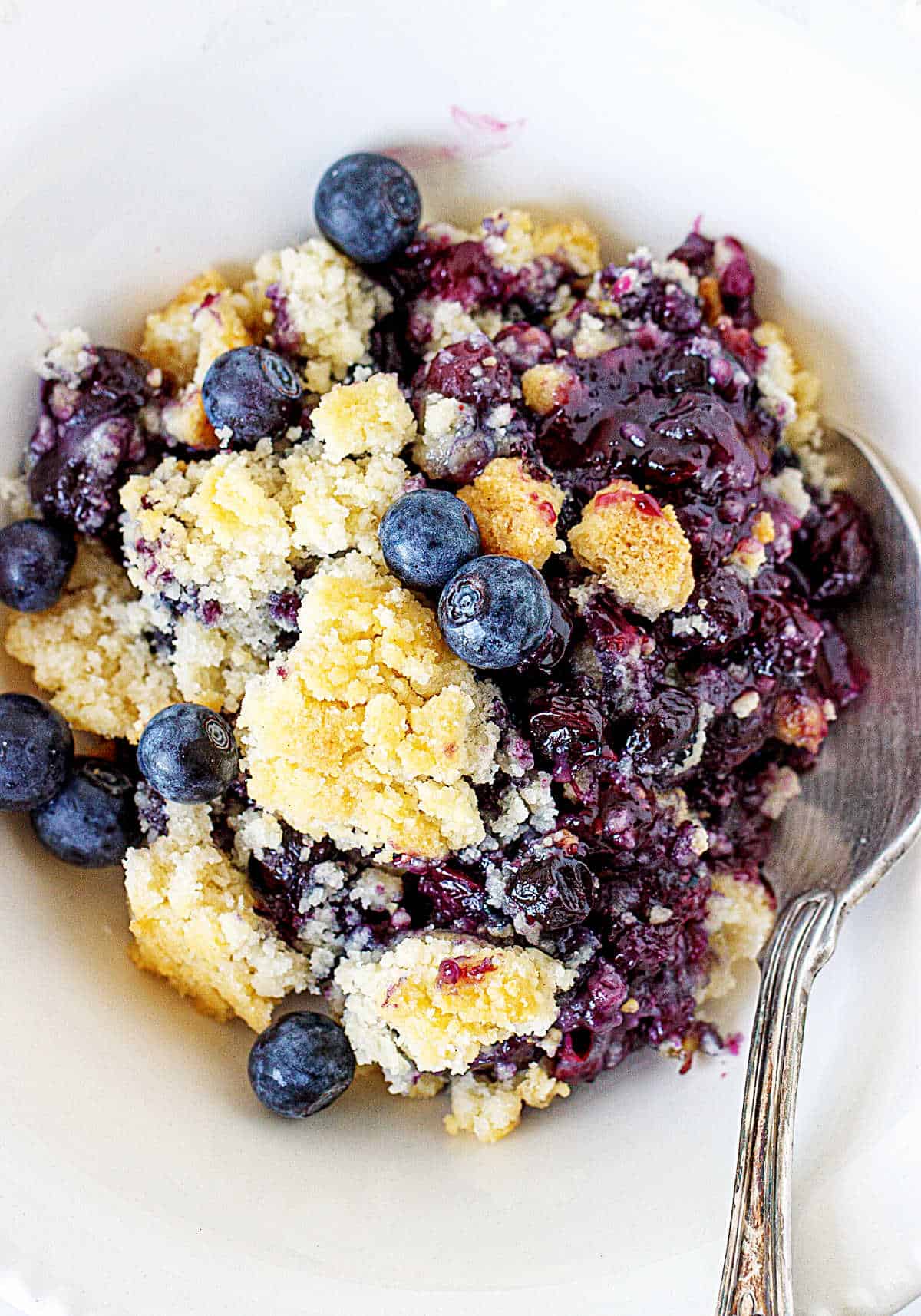 Overview of white bowl with spoon and serving of blueberry dump cake